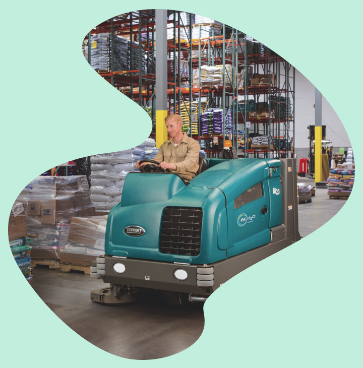 Industrial floor cleaning equipment by industry used in a warehouse, featuring a ride-on floor scrubber in action